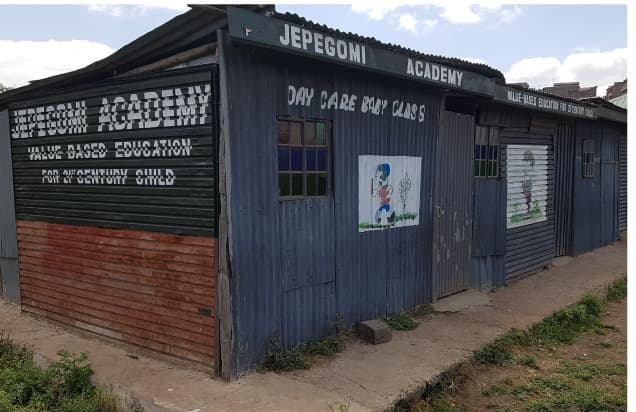 An iron-sheet building painted with the words Jepegomi Academy, Value Based Education, and Day Care Baby Class