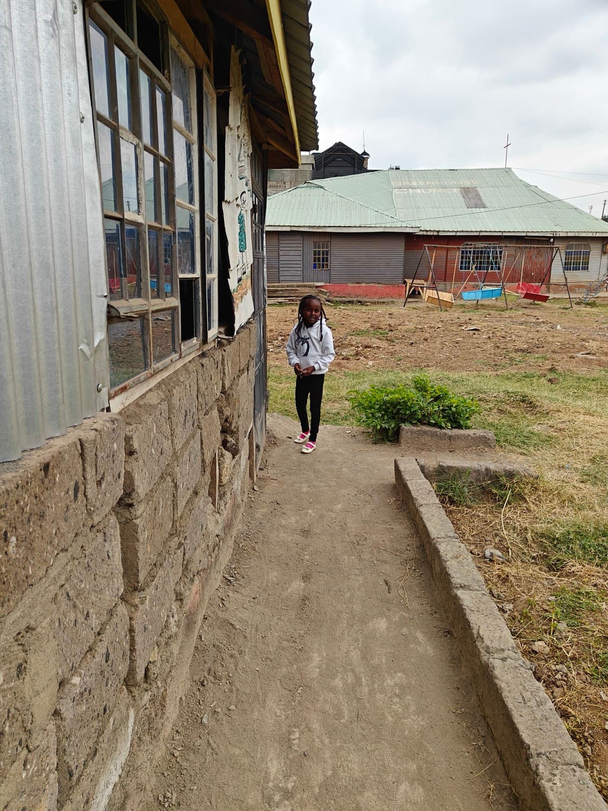 A child walking the concrete path between two classroom blocks, the church roof behind