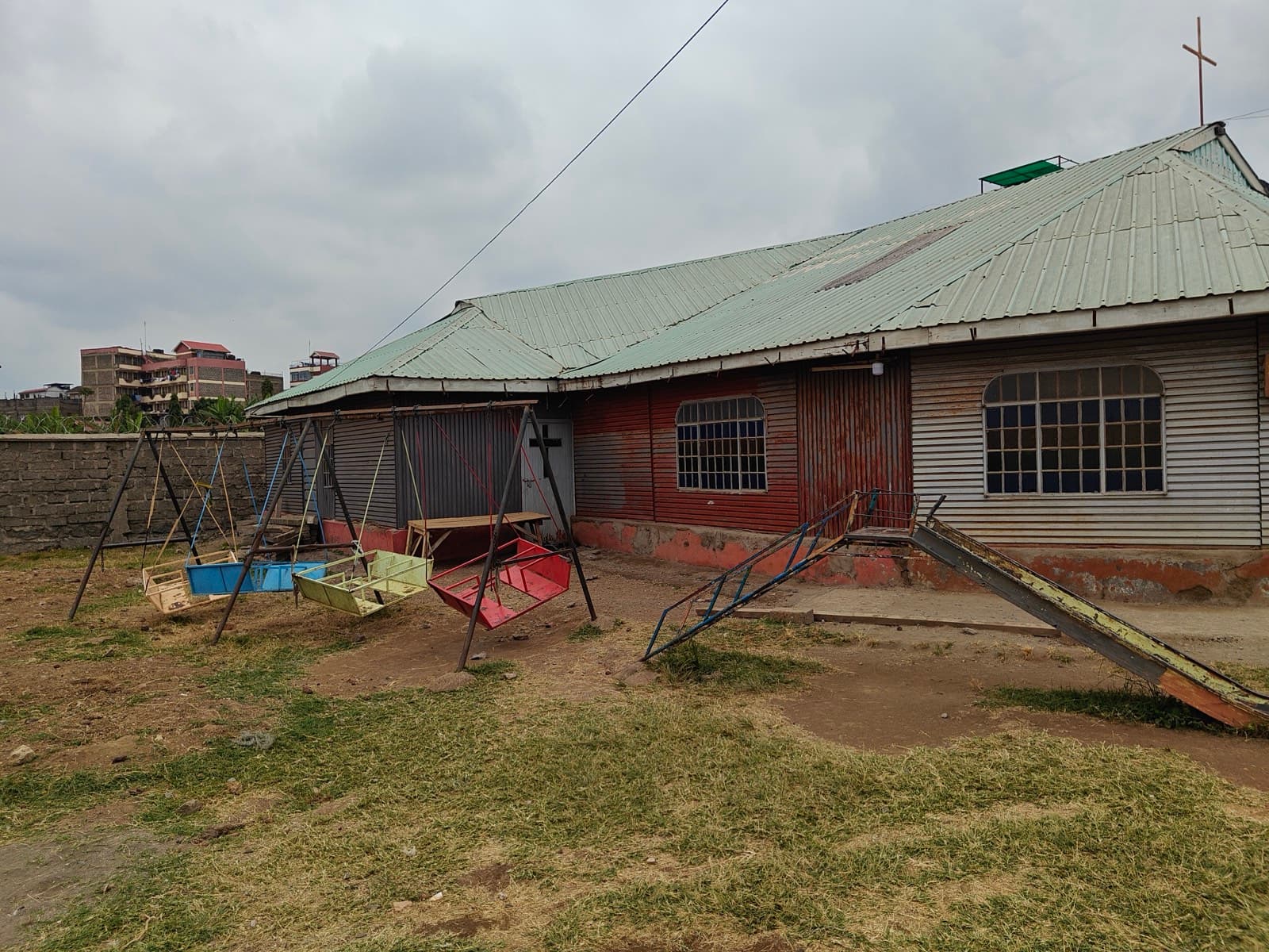 The sanctuary's green roof and red walls behind a swing frame and a see-saw on bare ground