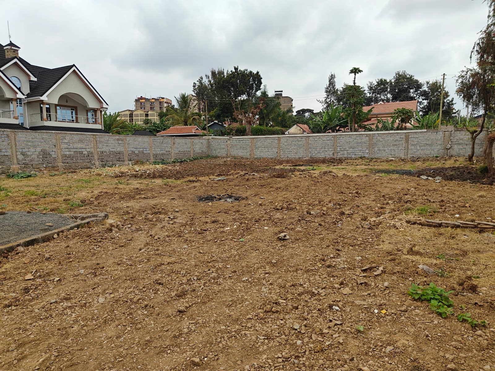 A cleared plot of bare ground enclosed by a stone perimeter wall, houses beyond it