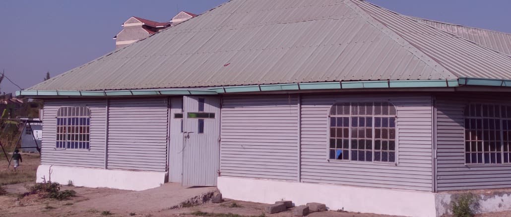 The semi-permanent sanctuary — a long iron-sheet building with a green roof and a cross above the door