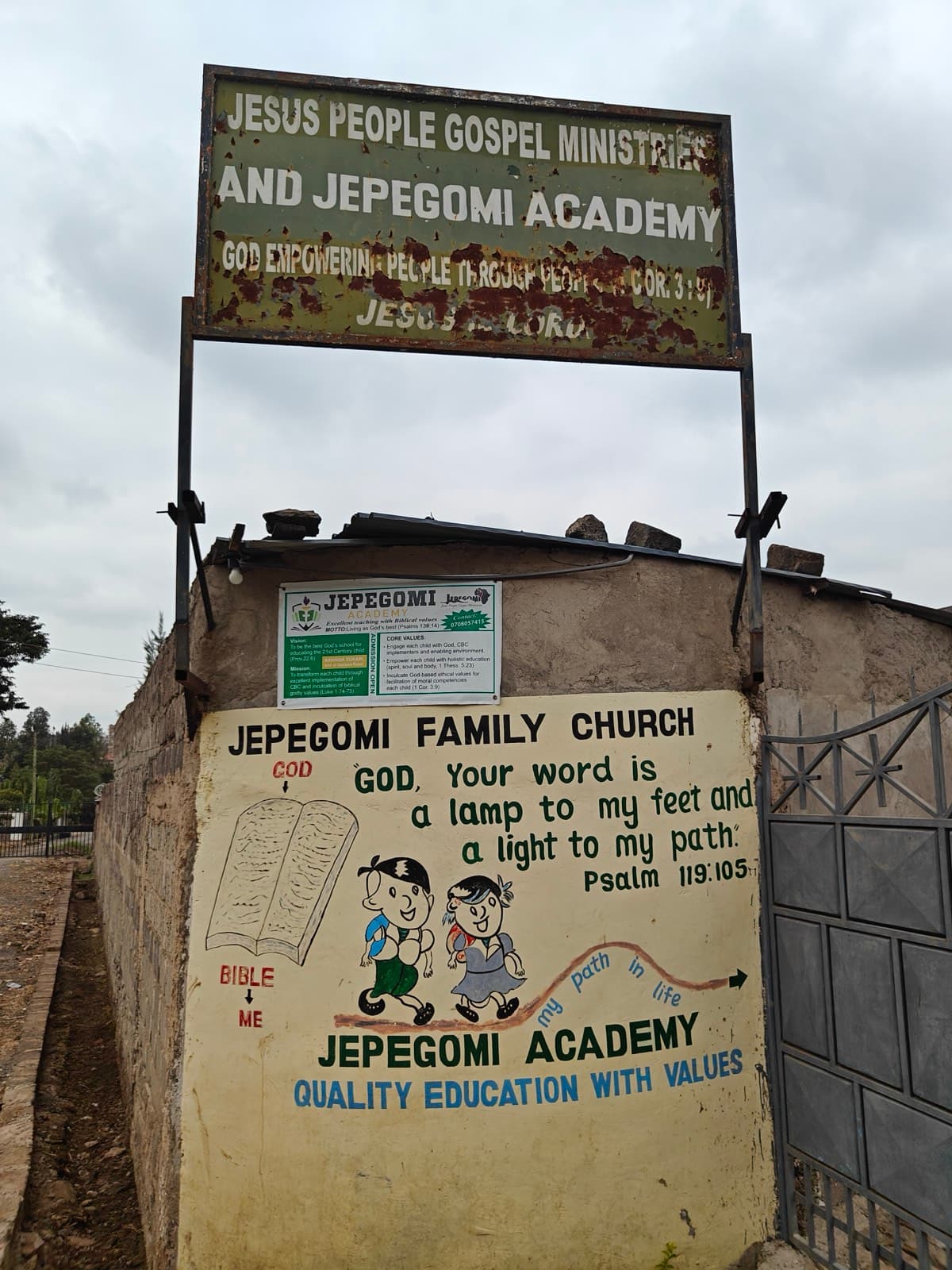 A weathered painted wall reading Jepegomi Family Church and Jepegomi Academy, Quality Education with Values, beneath a hand-lettered board