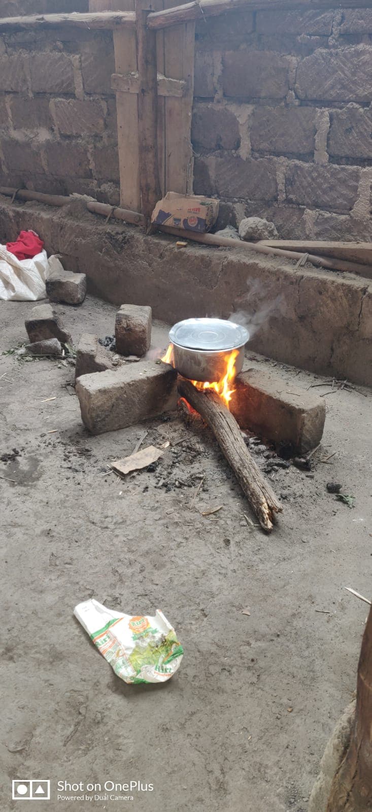 A cooking pot balanced on stones over an open wood fire on bare ground