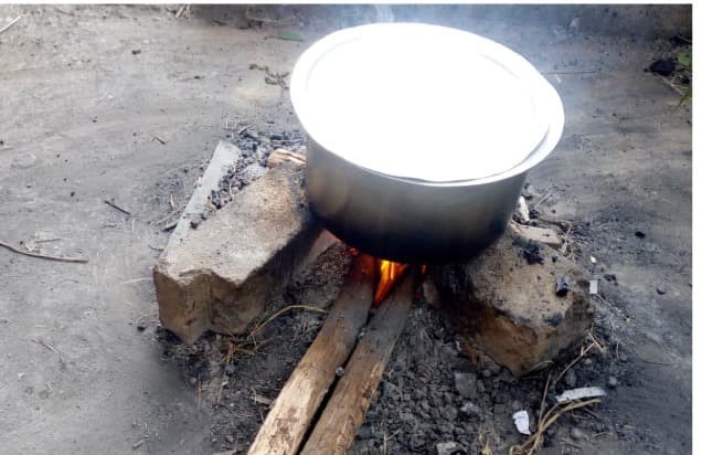 A large cooking pot balanced on stones over a wood fire on bare ground
