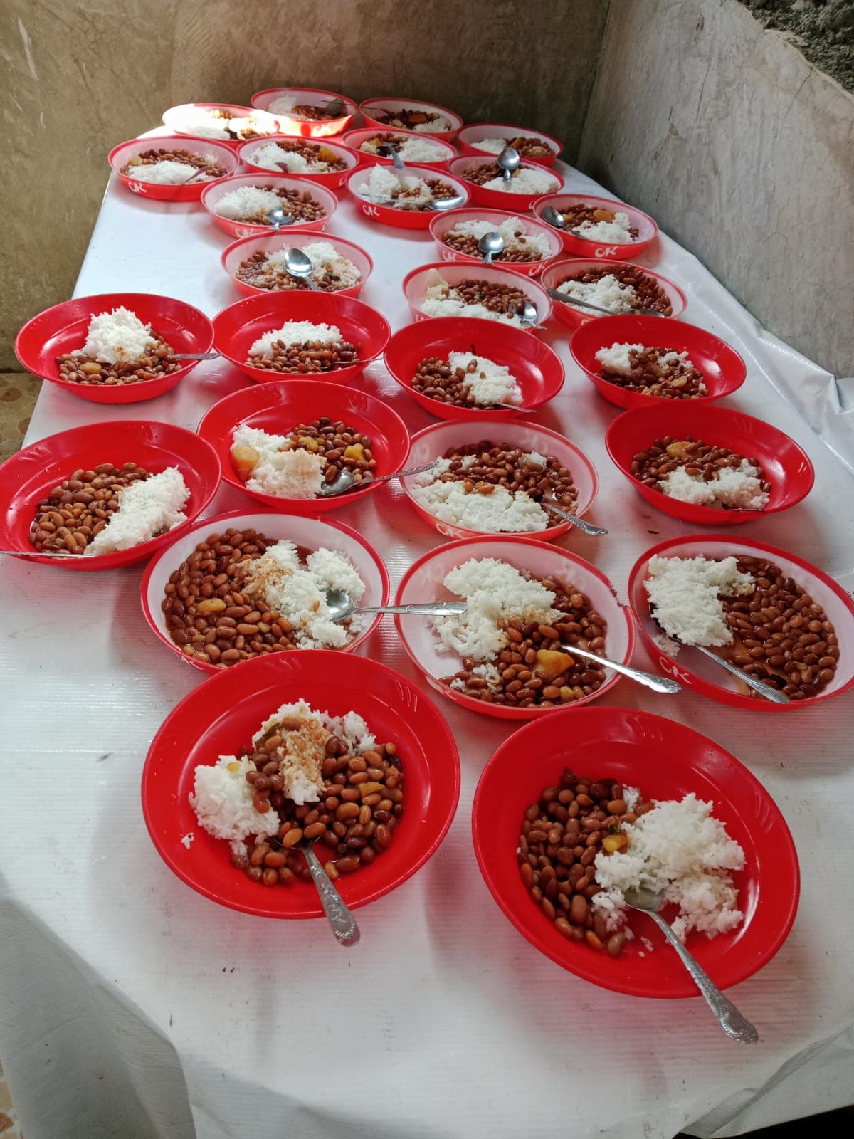 Rows of red plates filled with rice and beans, laid out ready for the children
