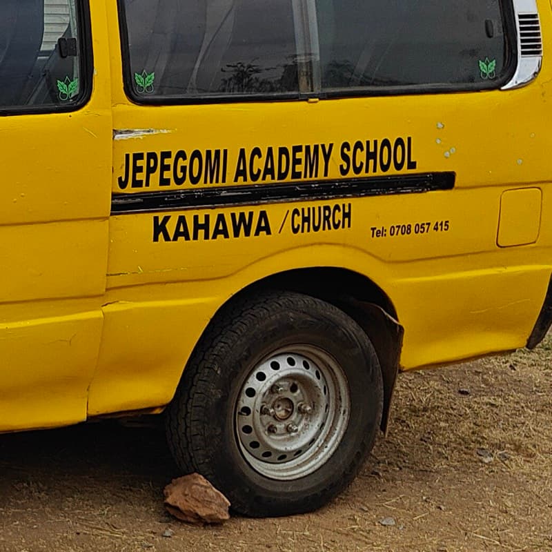 The van's side, lettered Jepegomi Academy School, Kahawa, Church — a stone chocked against the wheel