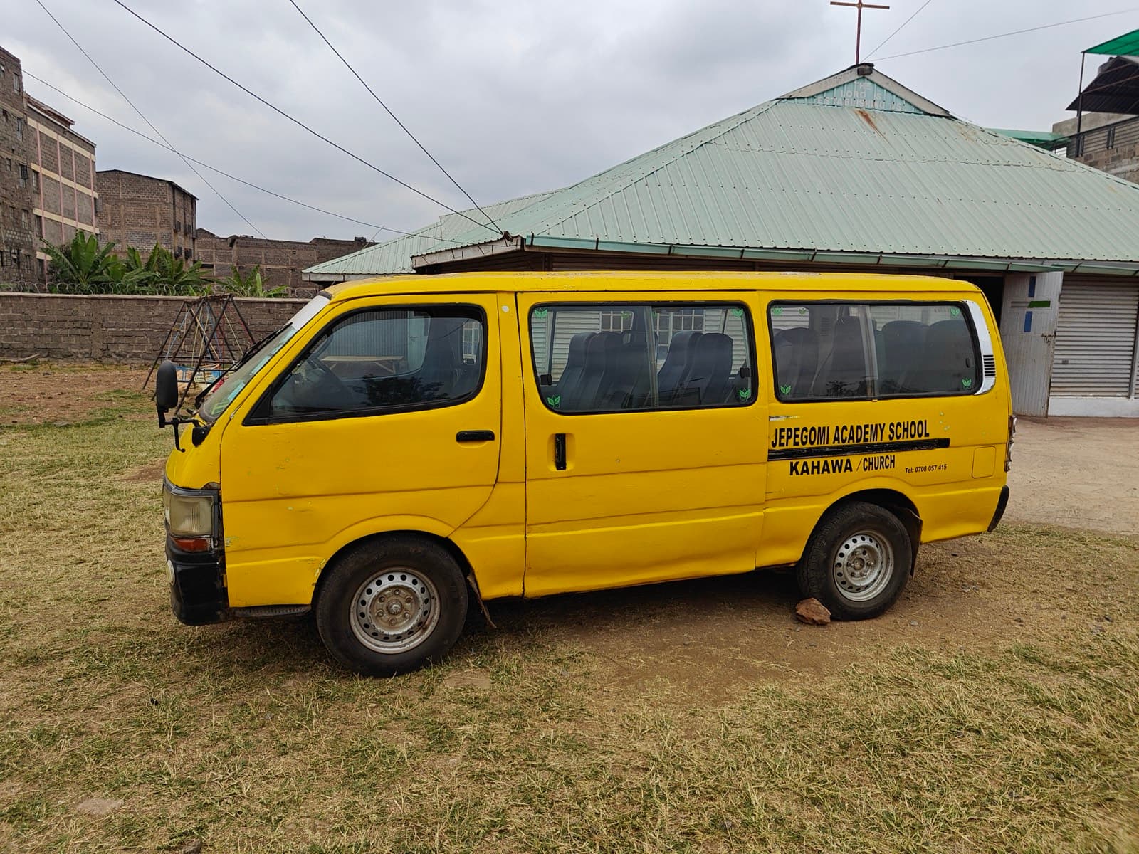 The academy's yellow school van parked on grass beside the church